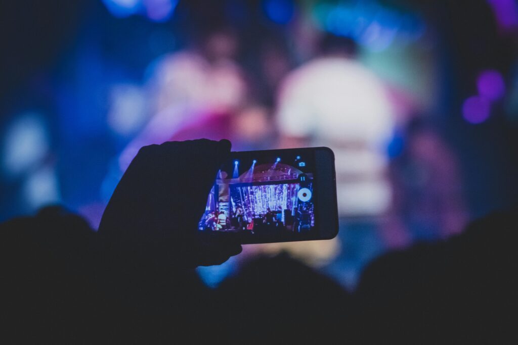 pexels-photo-1654691-1654691 A hand holds a smartphone recording a live concert with vibrant lights.