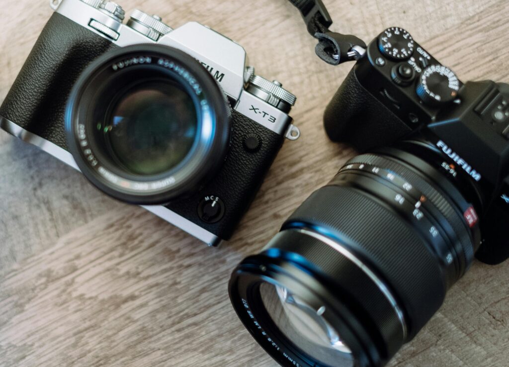 pexels-photo-3497060-3497060 Close-up of two mirrorless cameras with lenses on a wooden background, showcasing vintage style and design.